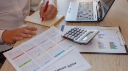 Woman doing paperwork with calculator and laptop